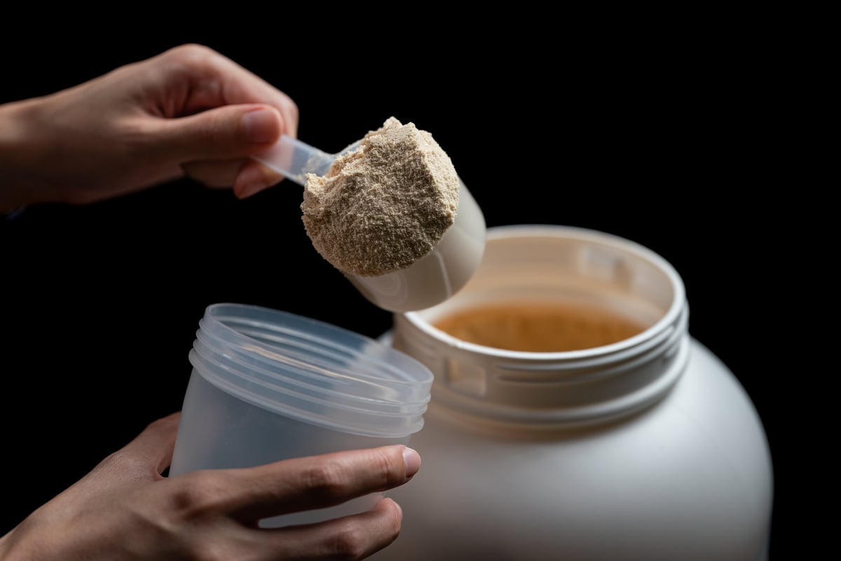 Closeup of Hand Measuring Scoop of Whey Protein and Shake